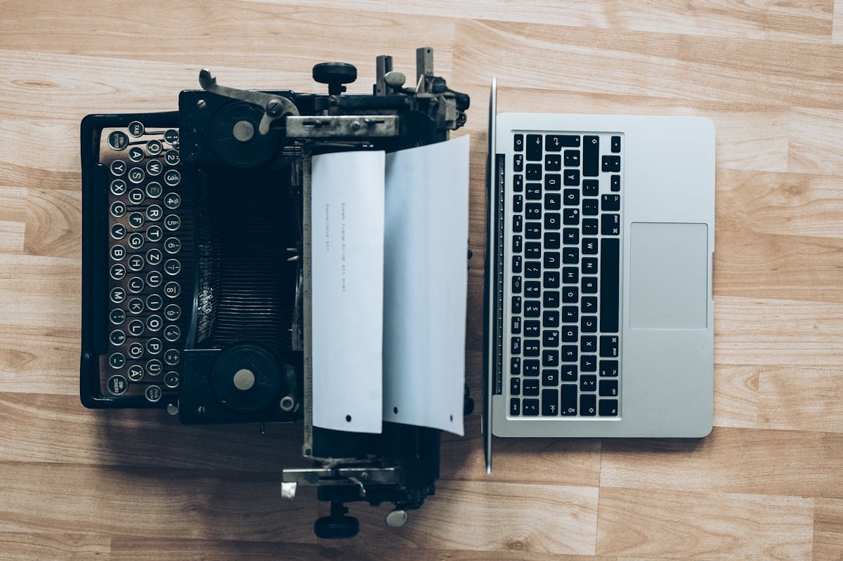 A type writer side by side with a Mac computer notebook