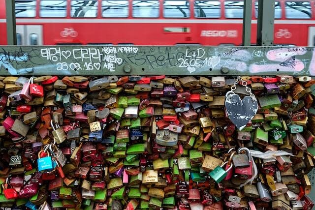 a wall covered in padlocks with a red double decker bus in the background