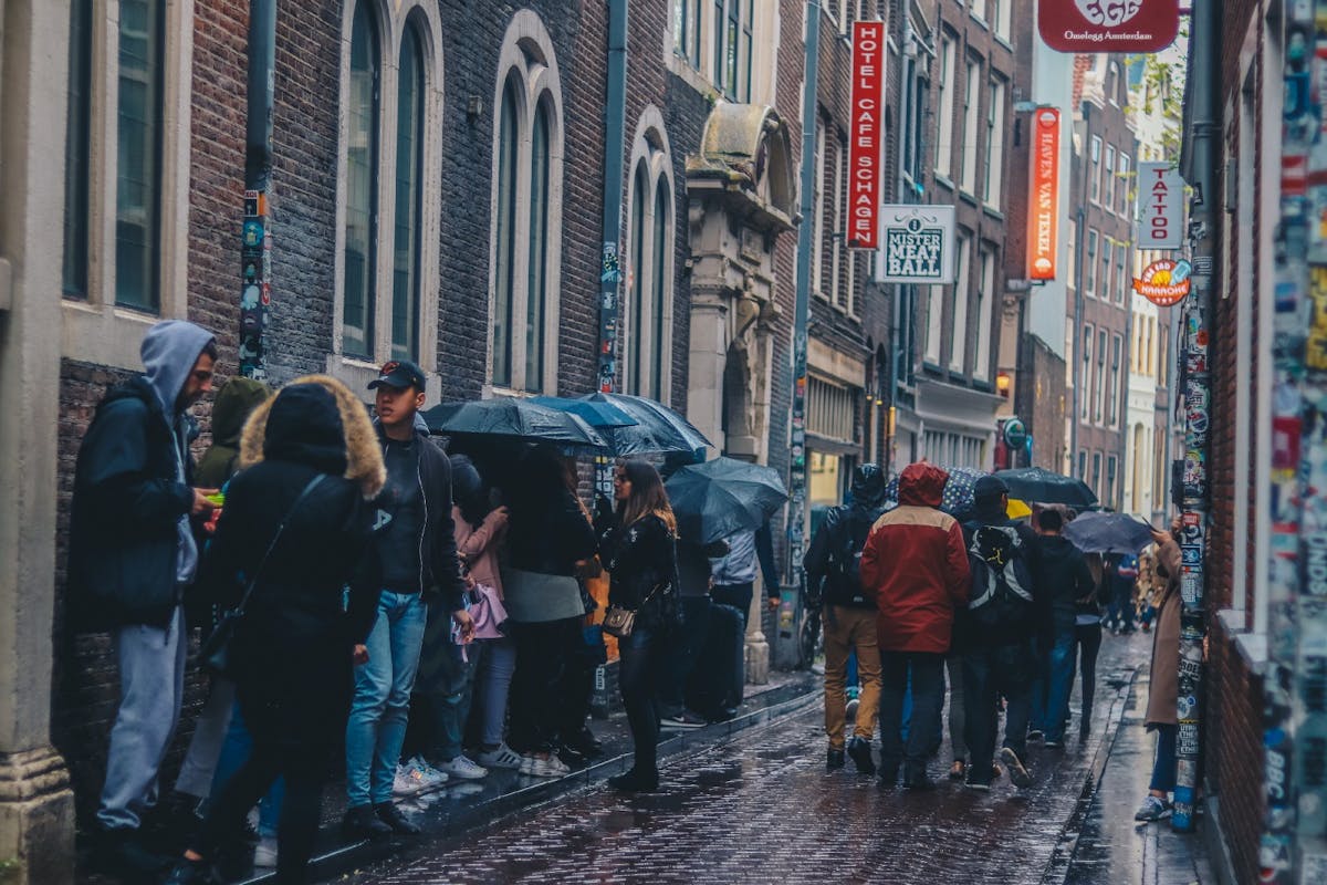 A narrow stree with a queue of people in the rain